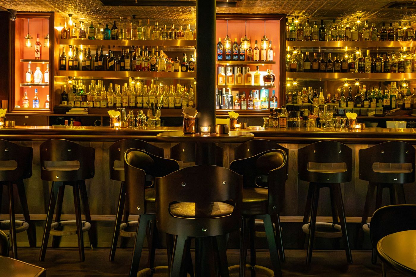 A back bar with lit shelving and a row of empty bar stools