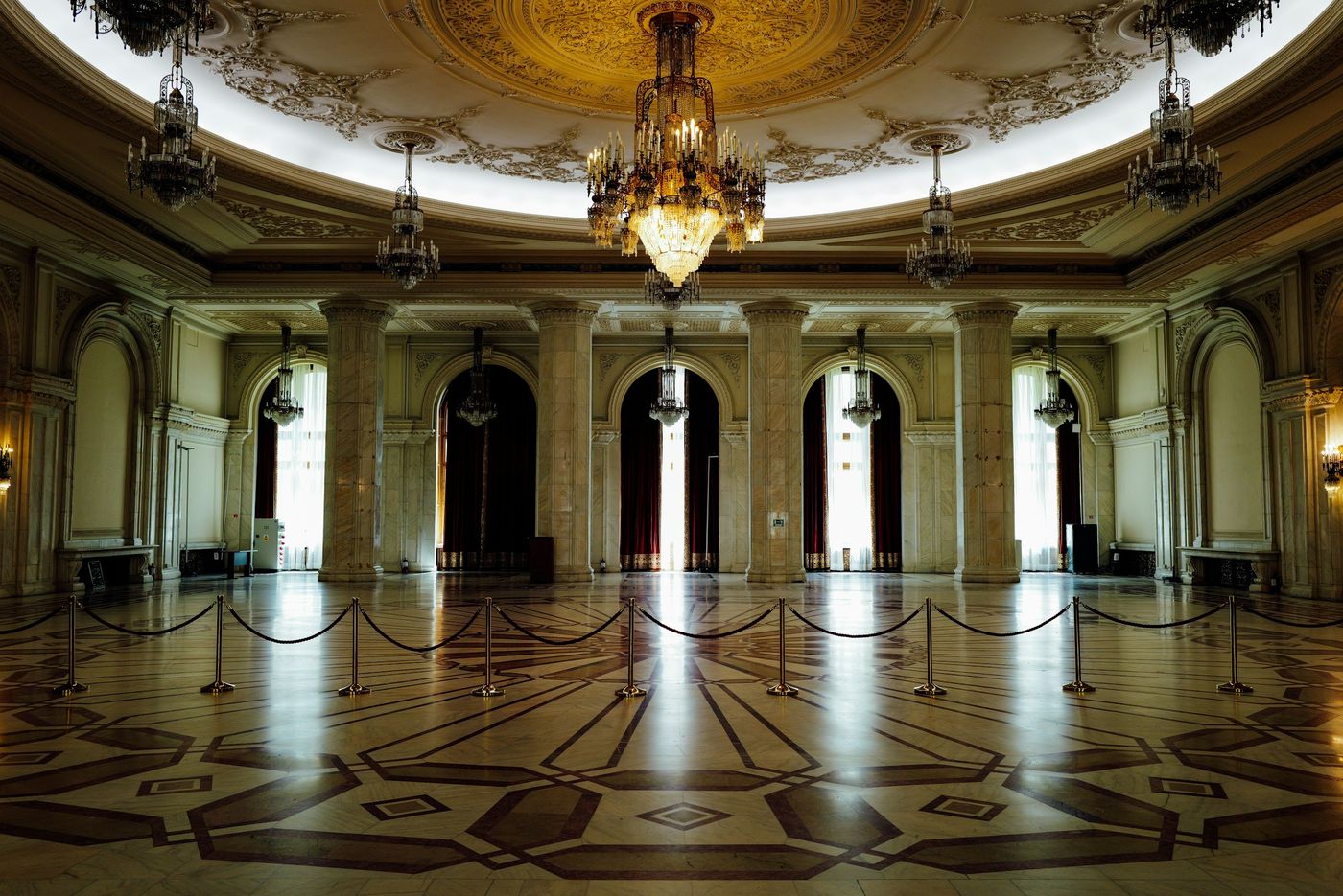 An empty ballroom with marble columns, chandeliers and a polished inlaid floor