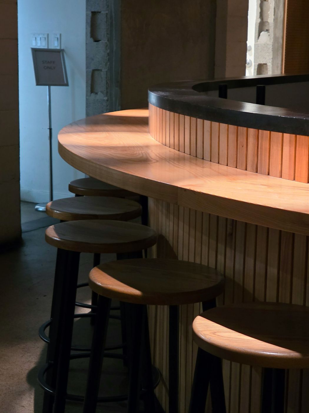A curved wooden bar with a row of empty stools