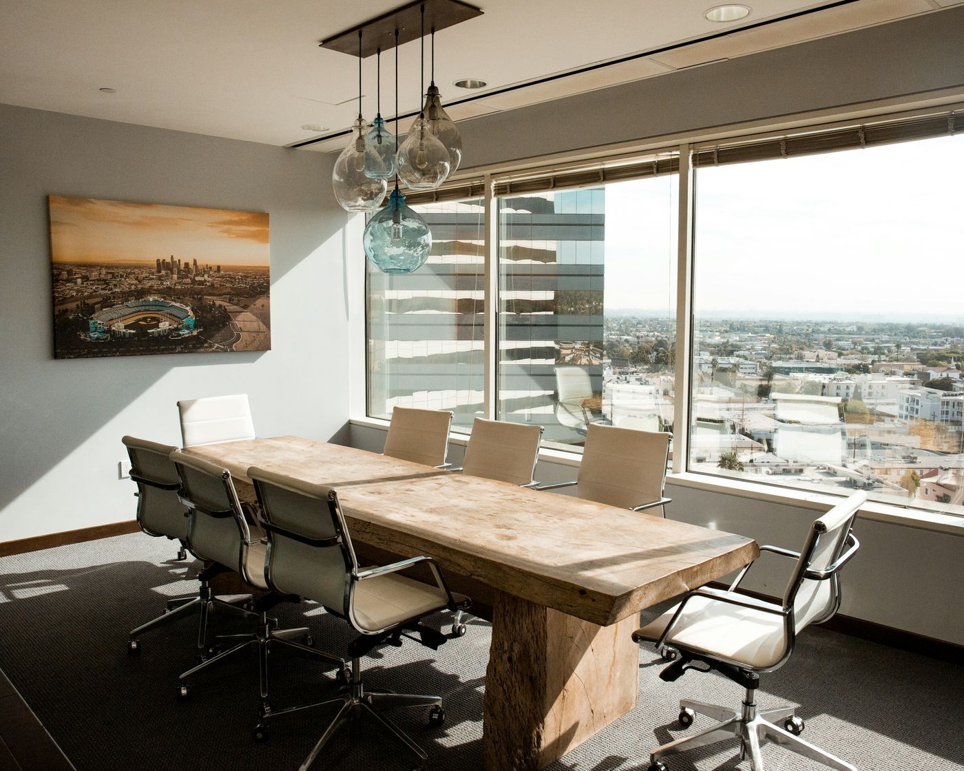 A conference room with a long wood table, white chairs and a city view