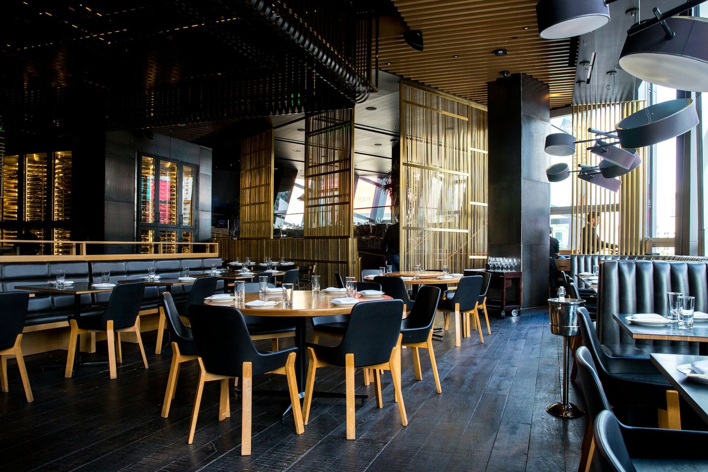 A restaurant dining room with leather booths, set tables and a dark wood floor