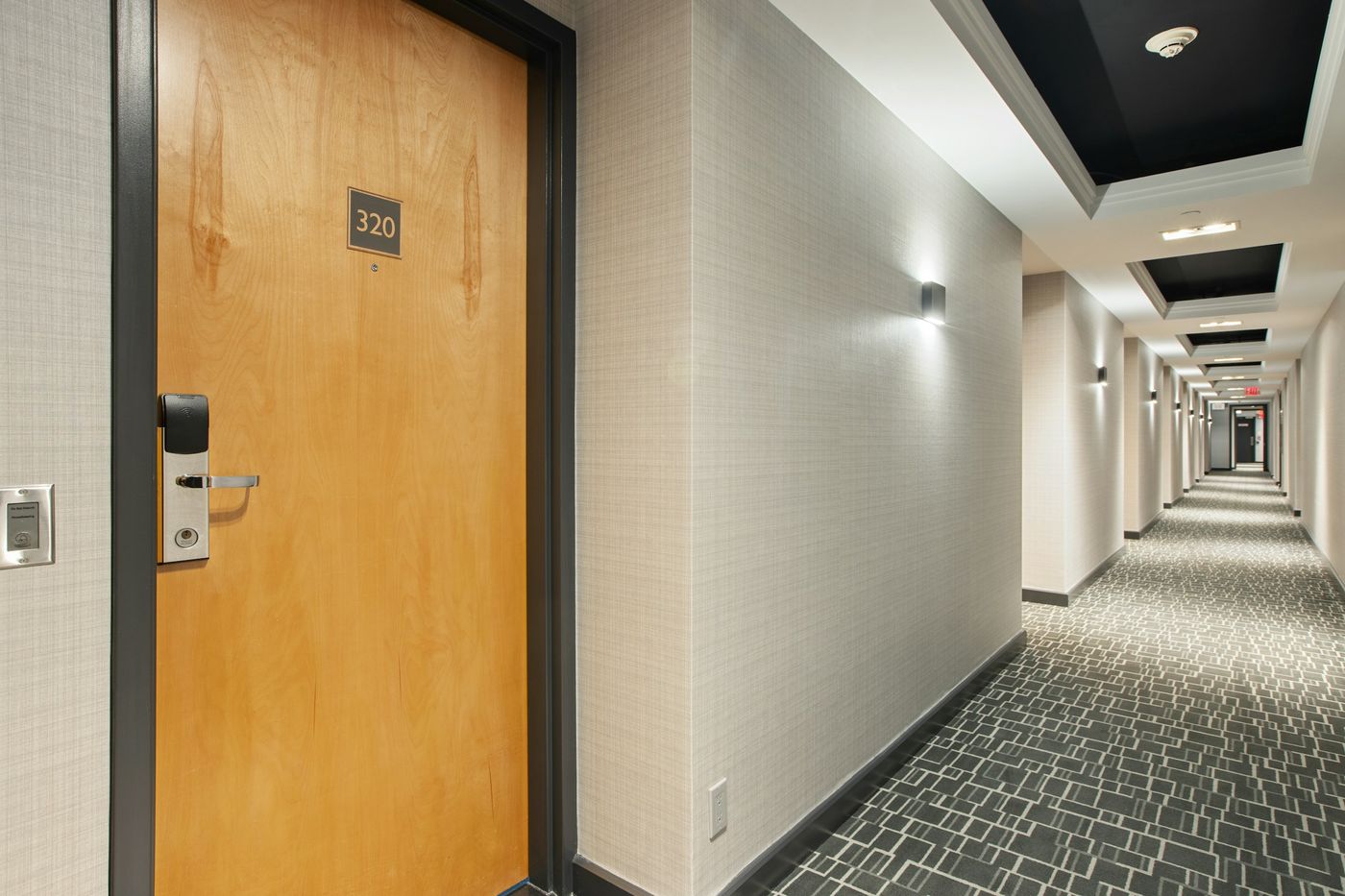A hotel corridor with a room door and patterned carpet