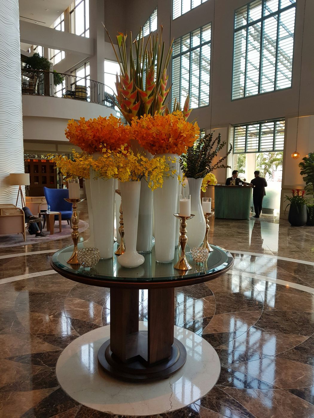 A hotel lobby with polished marble floors and a tall floral arrangement