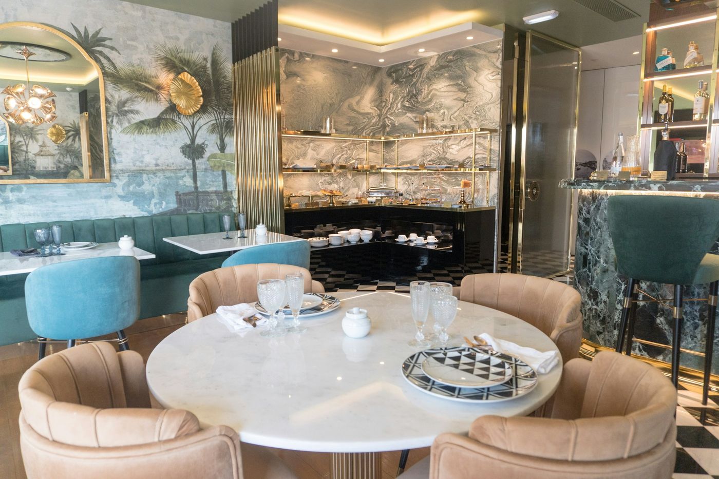 A hotel restaurant with banquette seating, a marble table set for breakfast and palm-print walls