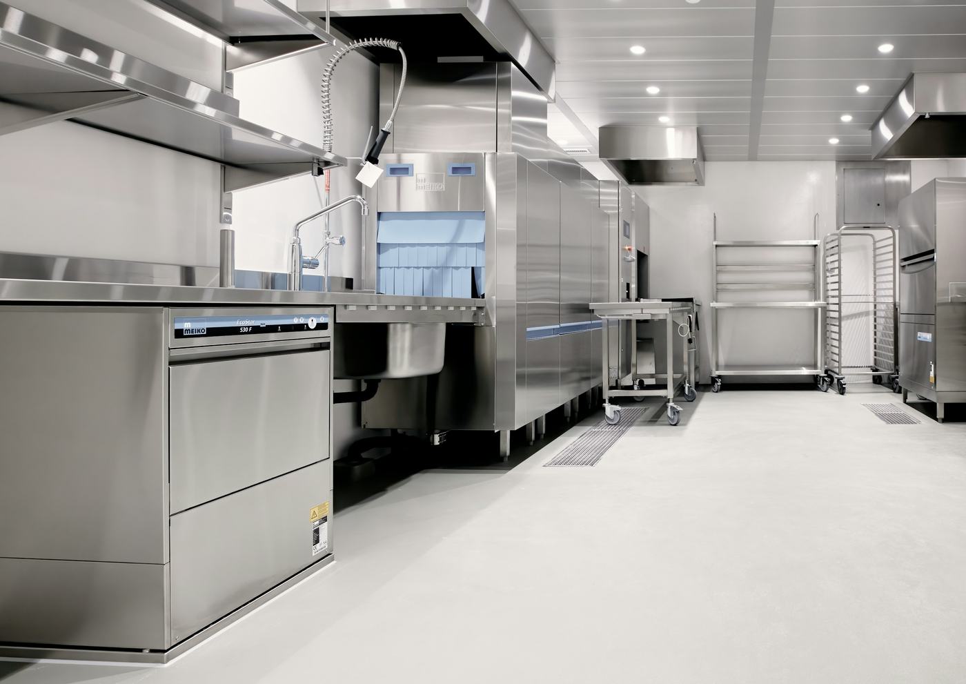 An empty commercial kitchen with a clean floor and drain grates