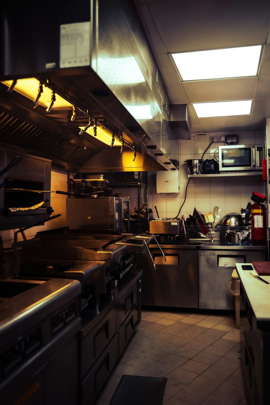 A commercial kitchen line with stainless hoods, ranges and a clean tiled floor