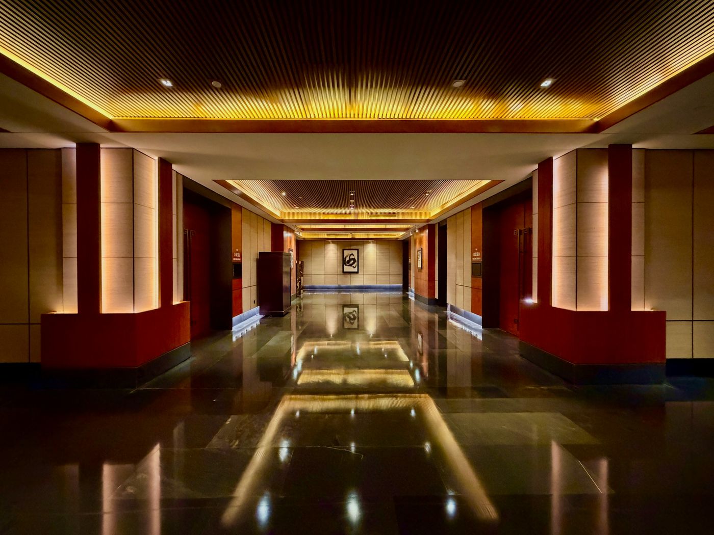 A long corridor with a polished stone floor reflecting the ceiling lights