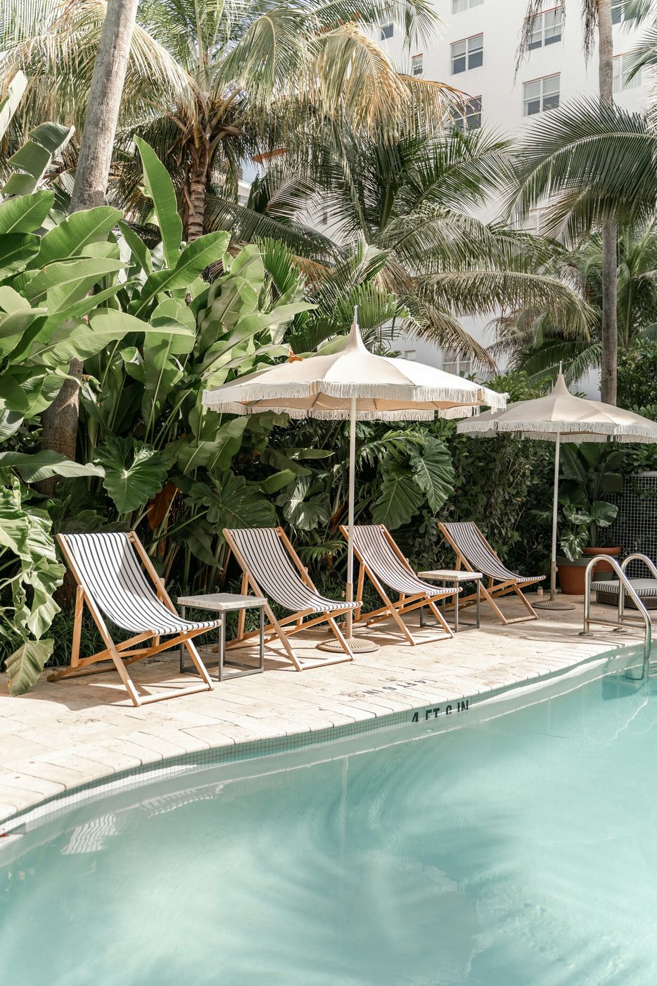 A resort pool with striped deck chairs and umbrellas under palm trees