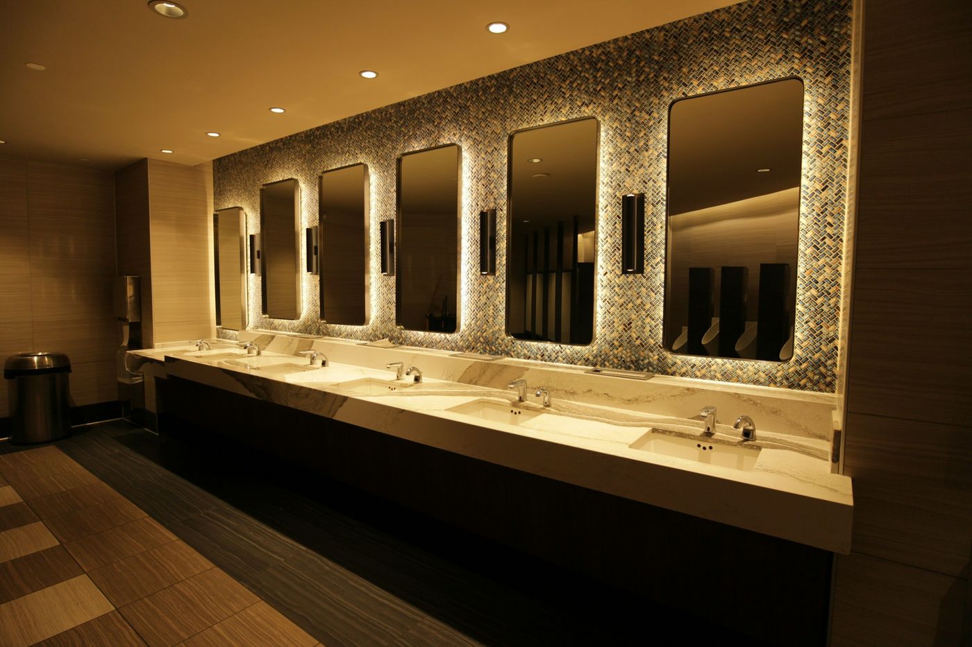 A restroom with a long stone vanity and lit mirrors